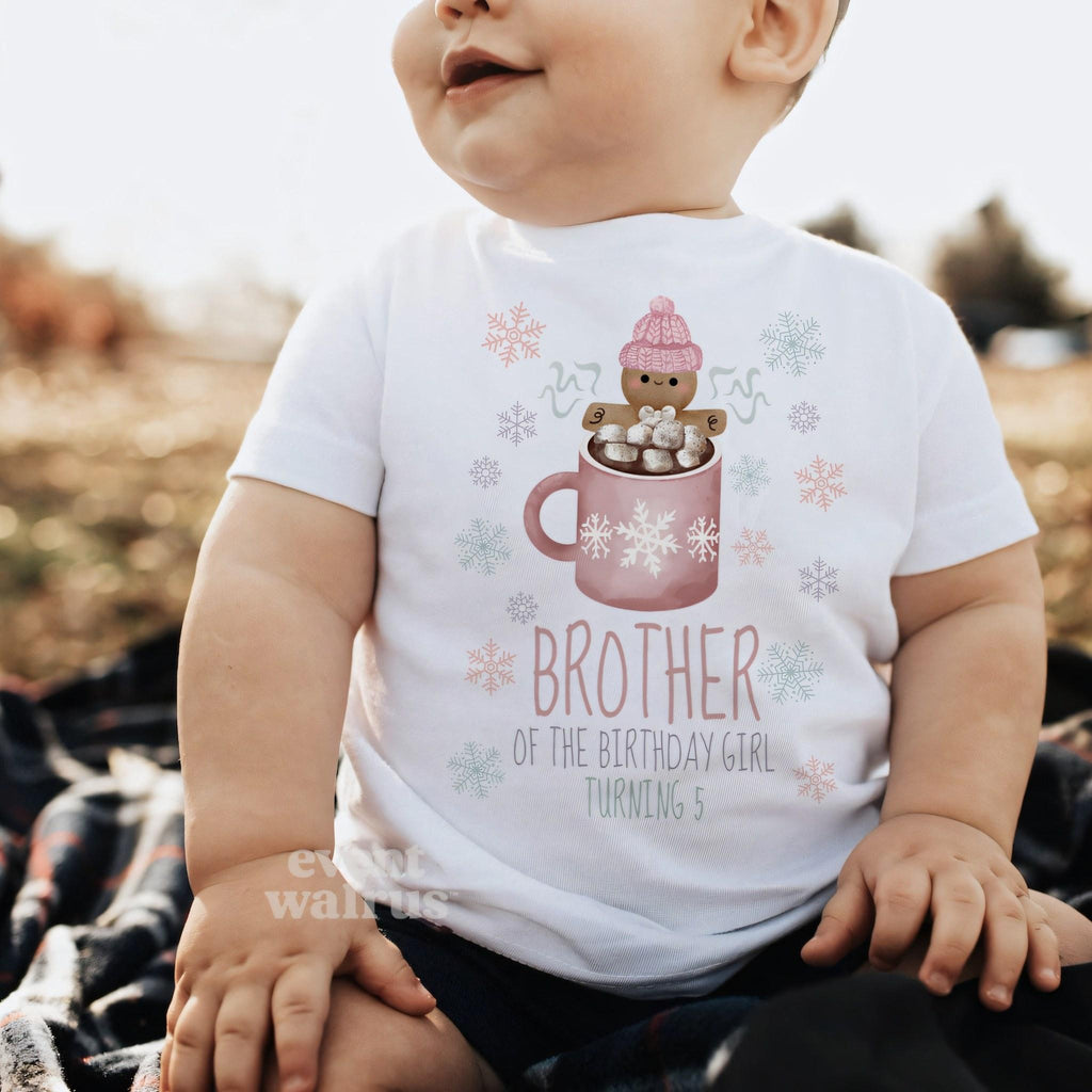 Baby sitting outdoors on a blanket in a white Brother of the Birthday Girl baby tee.