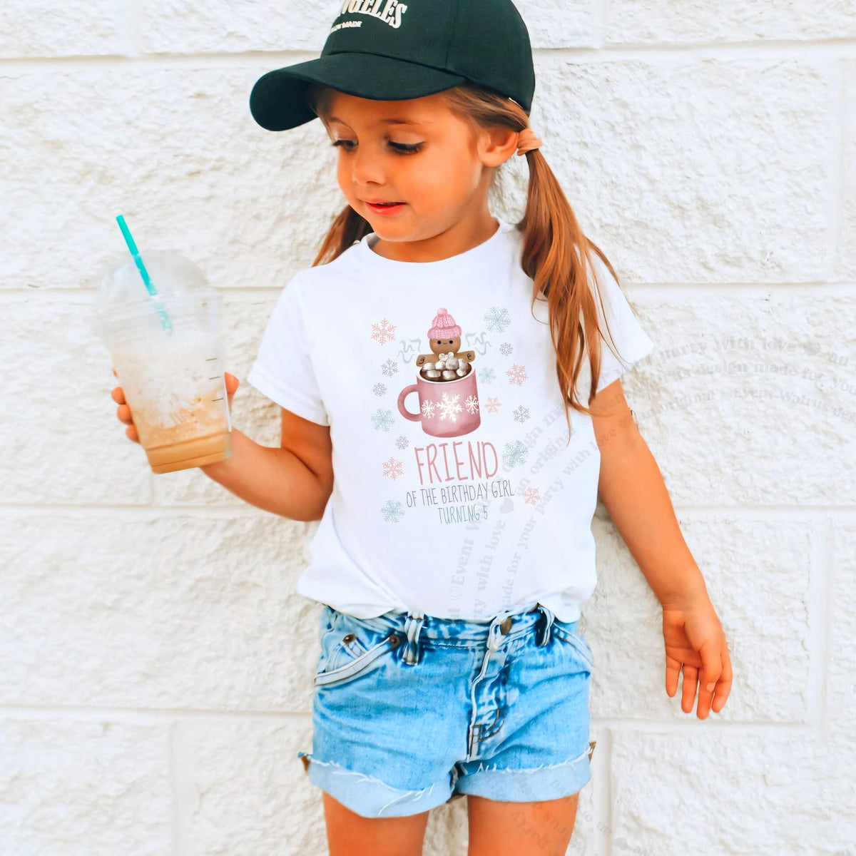 Girl in a ball cap holding a drink in a white pink Cookies and Cocoa Friend shirt.