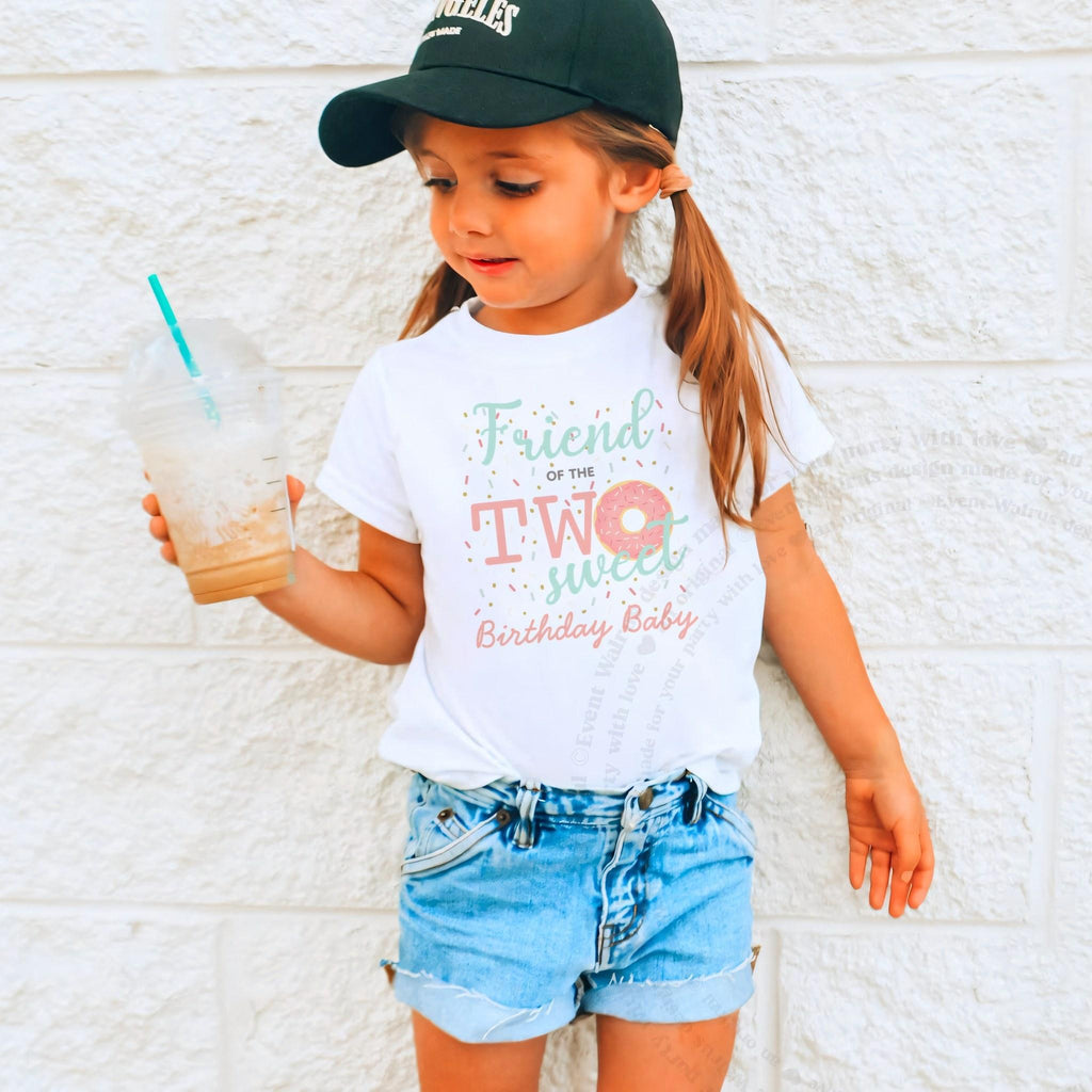 Girl in a ball cap holding a drink in a white Friend of the Two Sweet shirt.