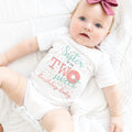 Baby girl with a pink bow lying in a white Sister of the Two Sweet bodysuit.