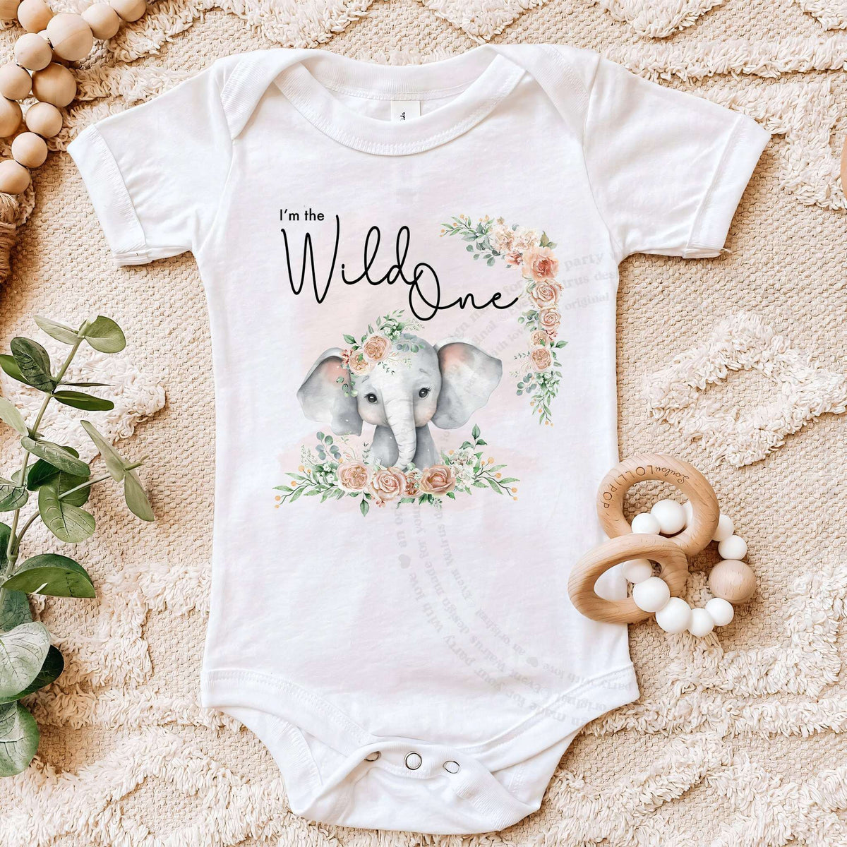 White I'm the Wild One bodysuit on a beige blanket with a wooden teether.