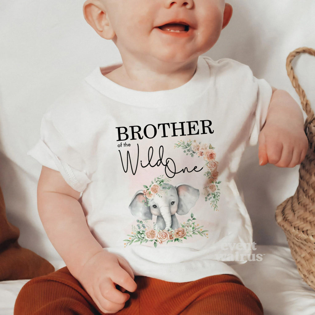 Baby sitting by a woven basket in a white Brother of the Wild One baby tee.