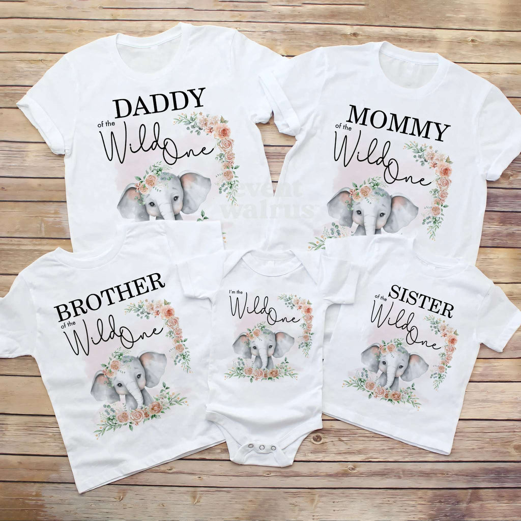 Daddy, Mommy, Brother, Sister and baby elephant Wild One shirts laid out on a wood table.
