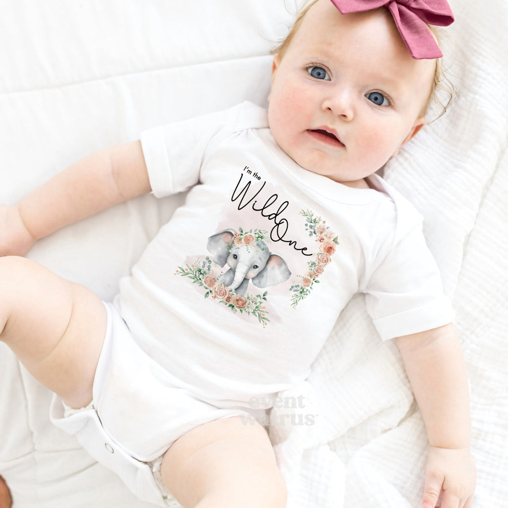Baby girl with a pink bow lying in a white I'm the Wild One elephant bodysuit.