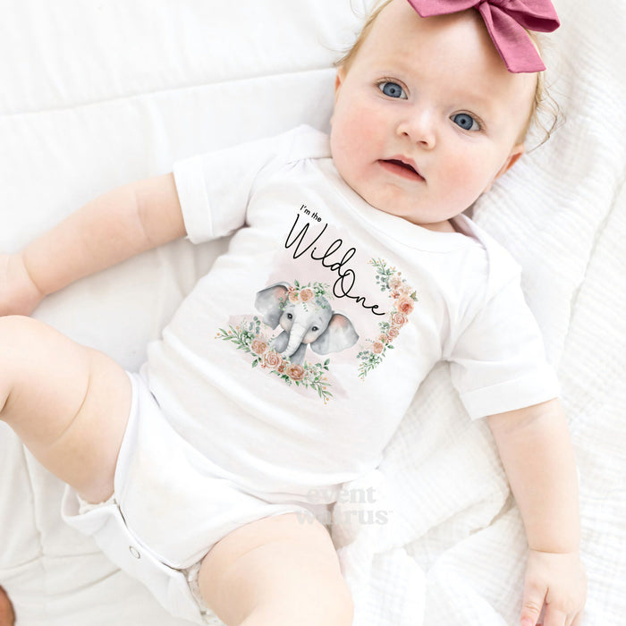 Baby girl with a pink bow lying in a white I'm the Wild One elephant bodysuit.