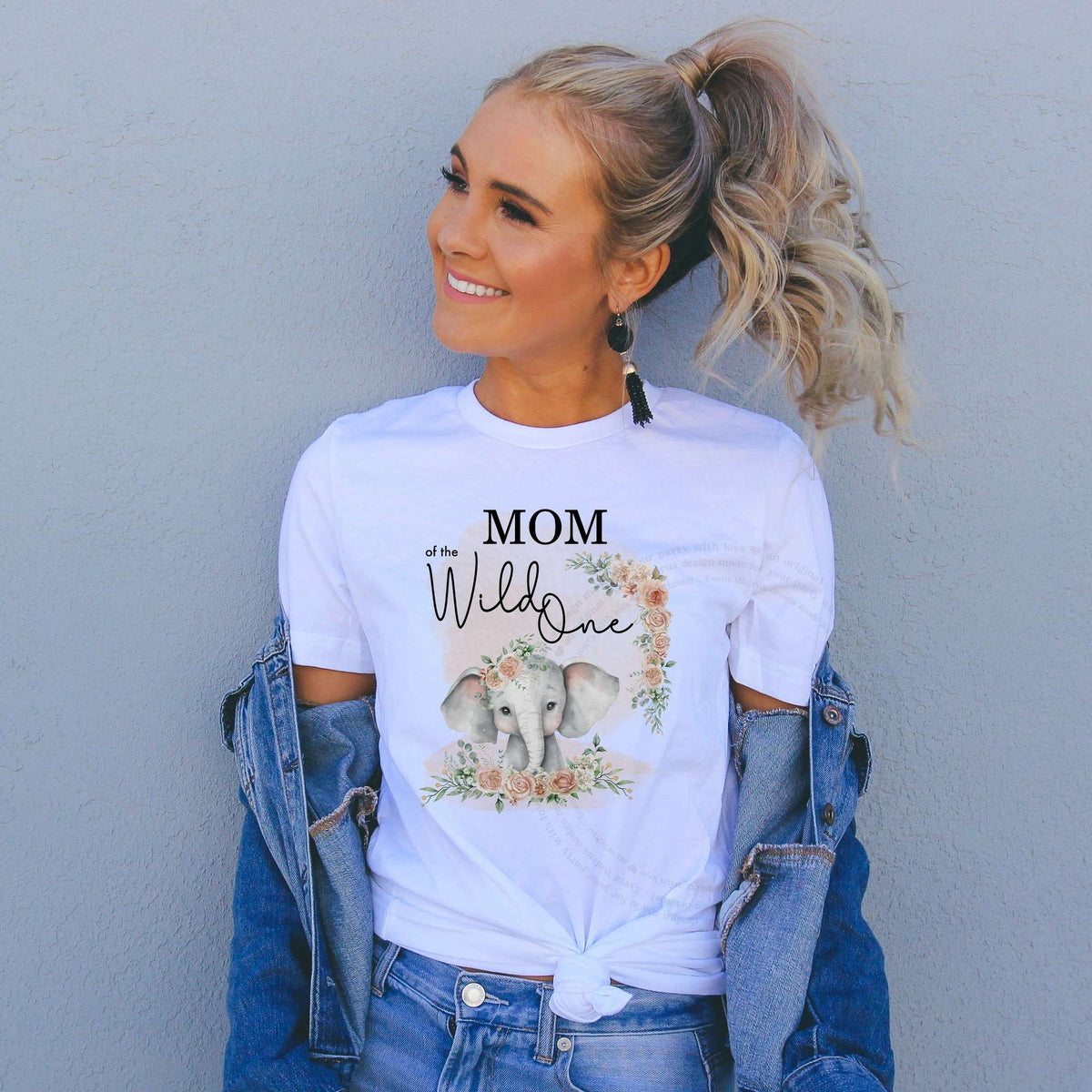 Woman in a denim jacket wearing a Mom of the Wild One shirt with a watercolor elephant.