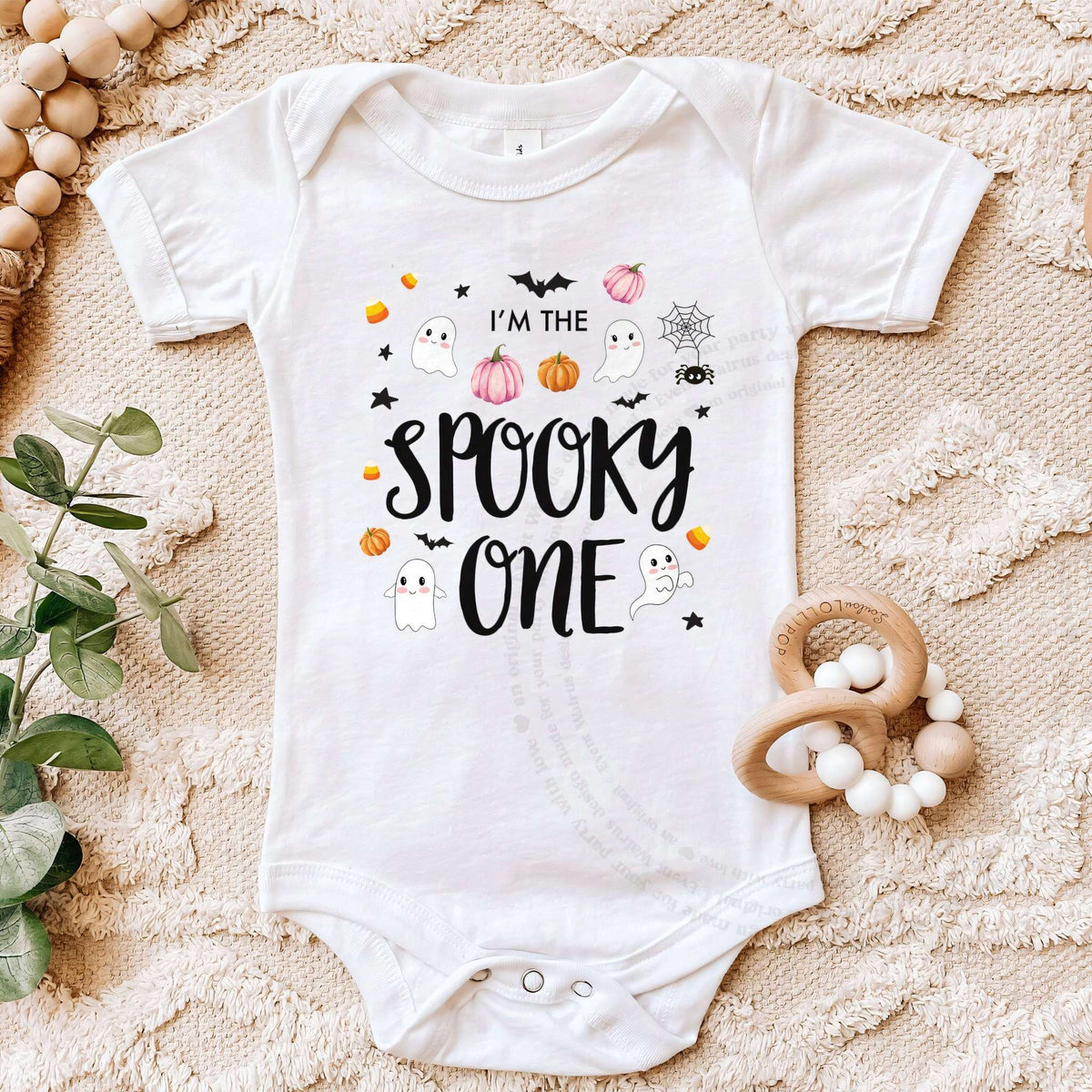 White I'm the Spooky One bodysuit on a beige blanket with a wooden teether.