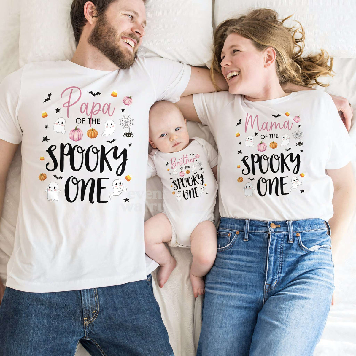 Baby in a Spooky One bodysuit lying between Papa and Mama in matching shirts.