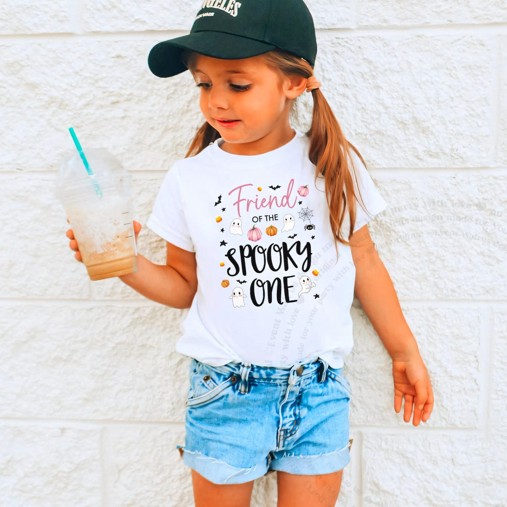 Girl in a ball cap holding a drink in a white Friend of the Spooky One shirt.