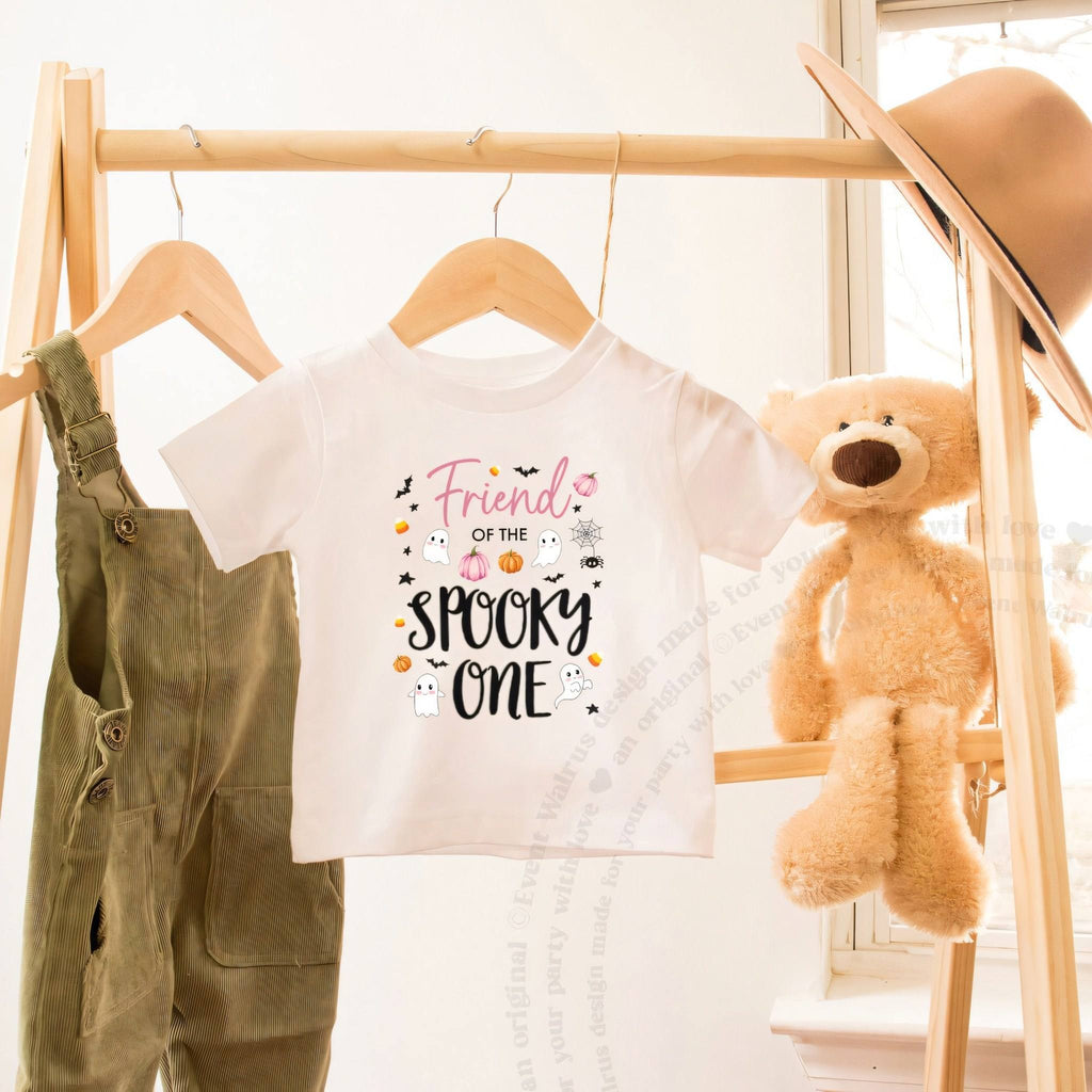 White Friend of the Spooky One toddler tee on a wooden clothes rack beside a teddy bear.