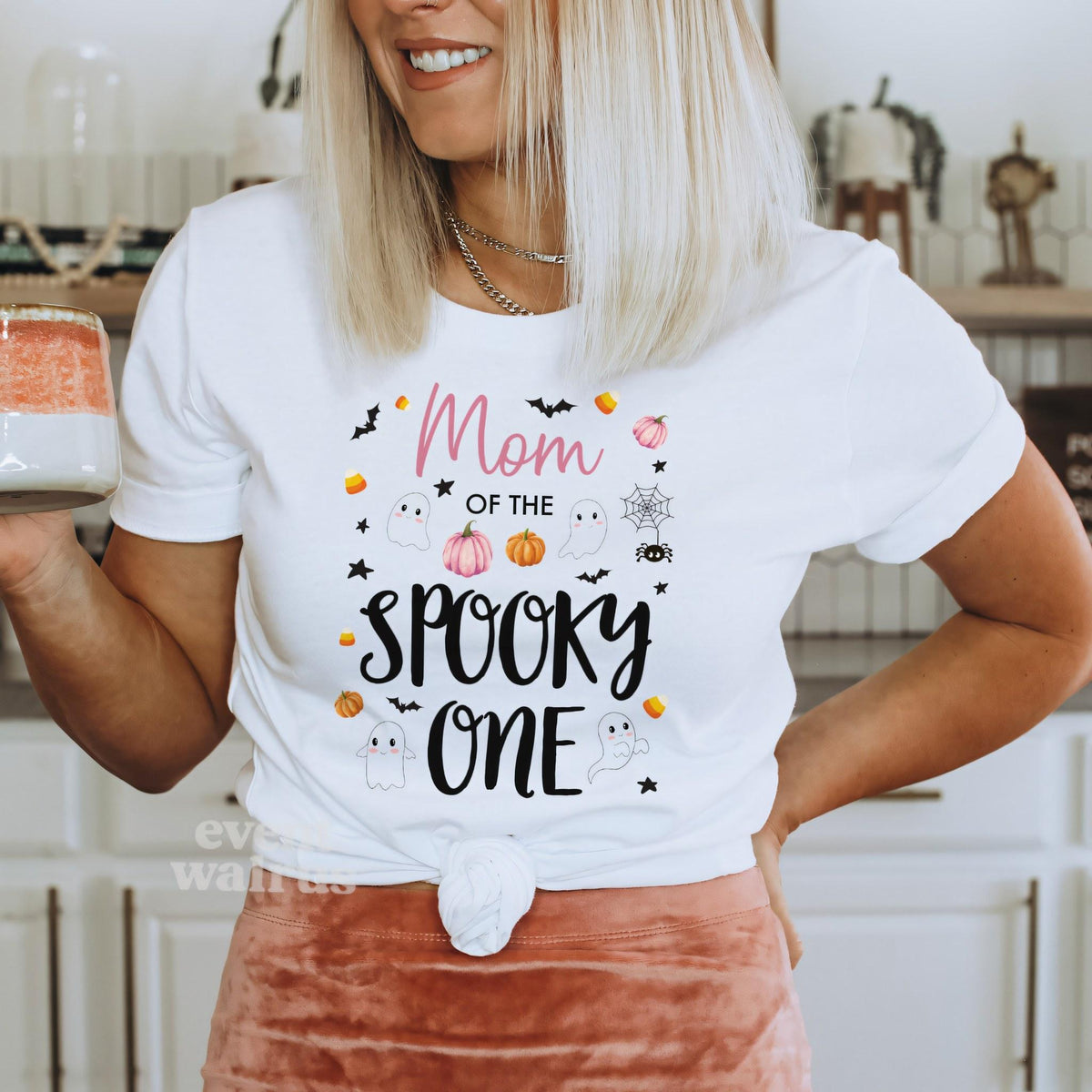 Woman holding a mug in a white Mom of the Spooky One shirt.