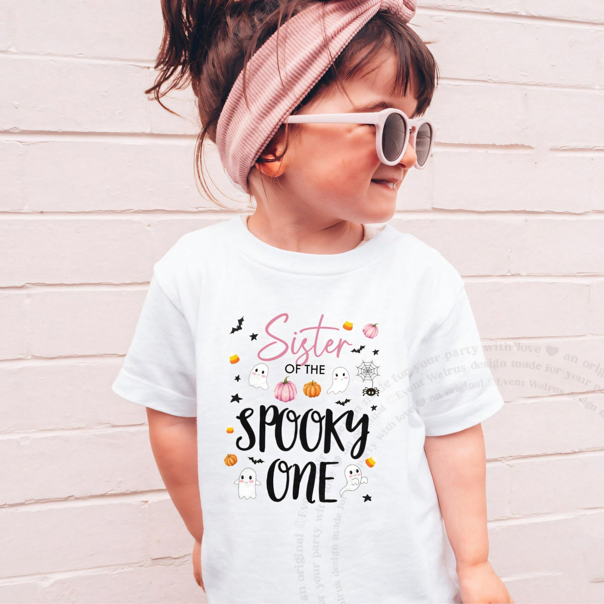 Girl in sunglasses and a pink headband wearing a white Sister of the Spooky One shirt.