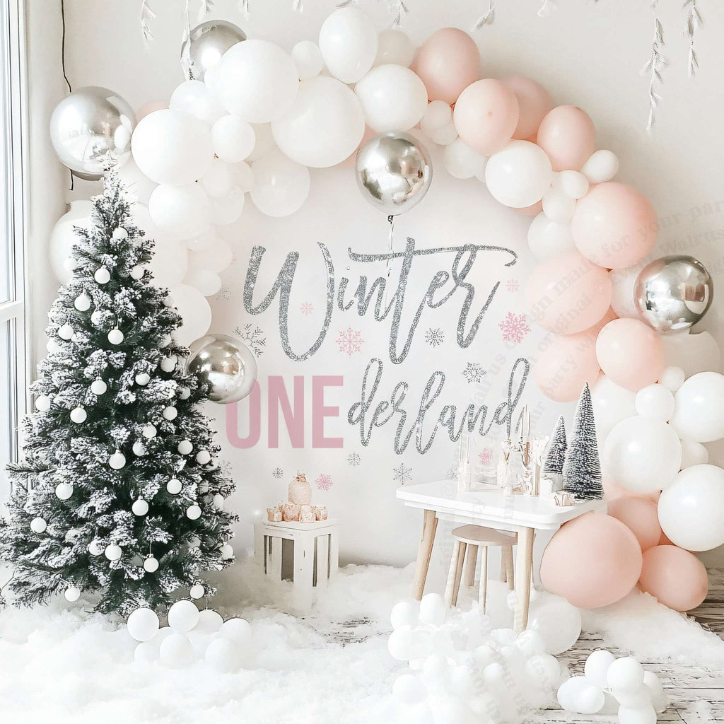 Pink winter onederland backdrop beside a flocked Christmas tree under a blush and white balloon arch.