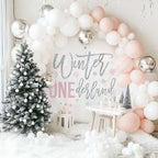 Pink winter onederland backdrop beside a flocked Christmas tree under a blush and white balloon arch.