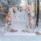 Pink glitter winter onederland backdrop in snowy woods with pink and silver balloons and lanterns.
