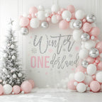 Glitter winter onederland backdrop in a white room with pink and silver balloons and a snowy tree.