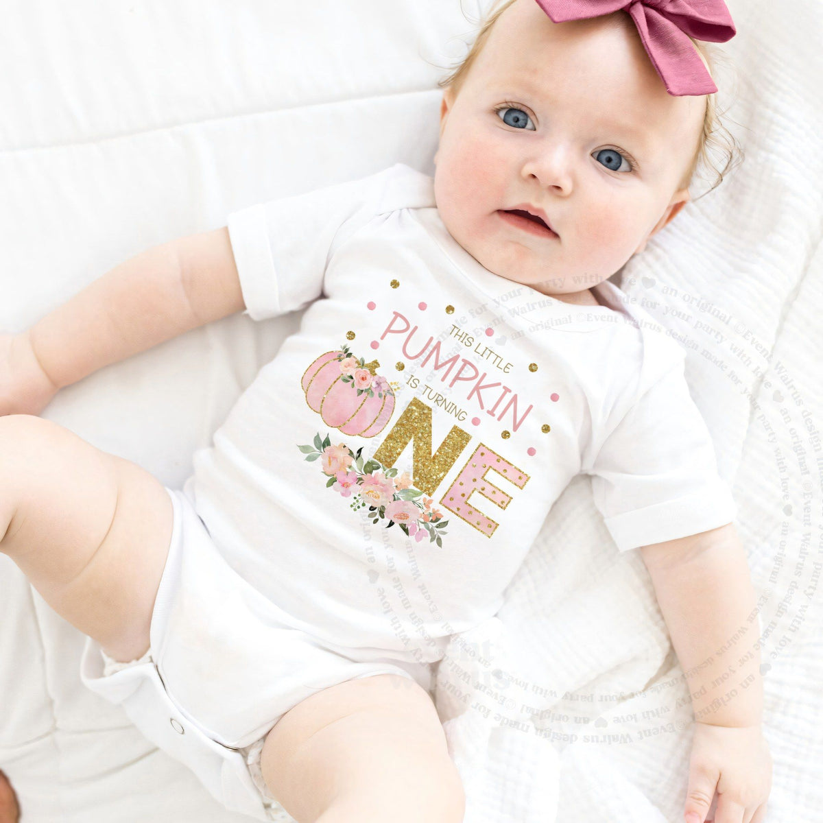 Baby girl with a pink bow lying in a white This Little Pumpkin Is Turning One bodysuit.