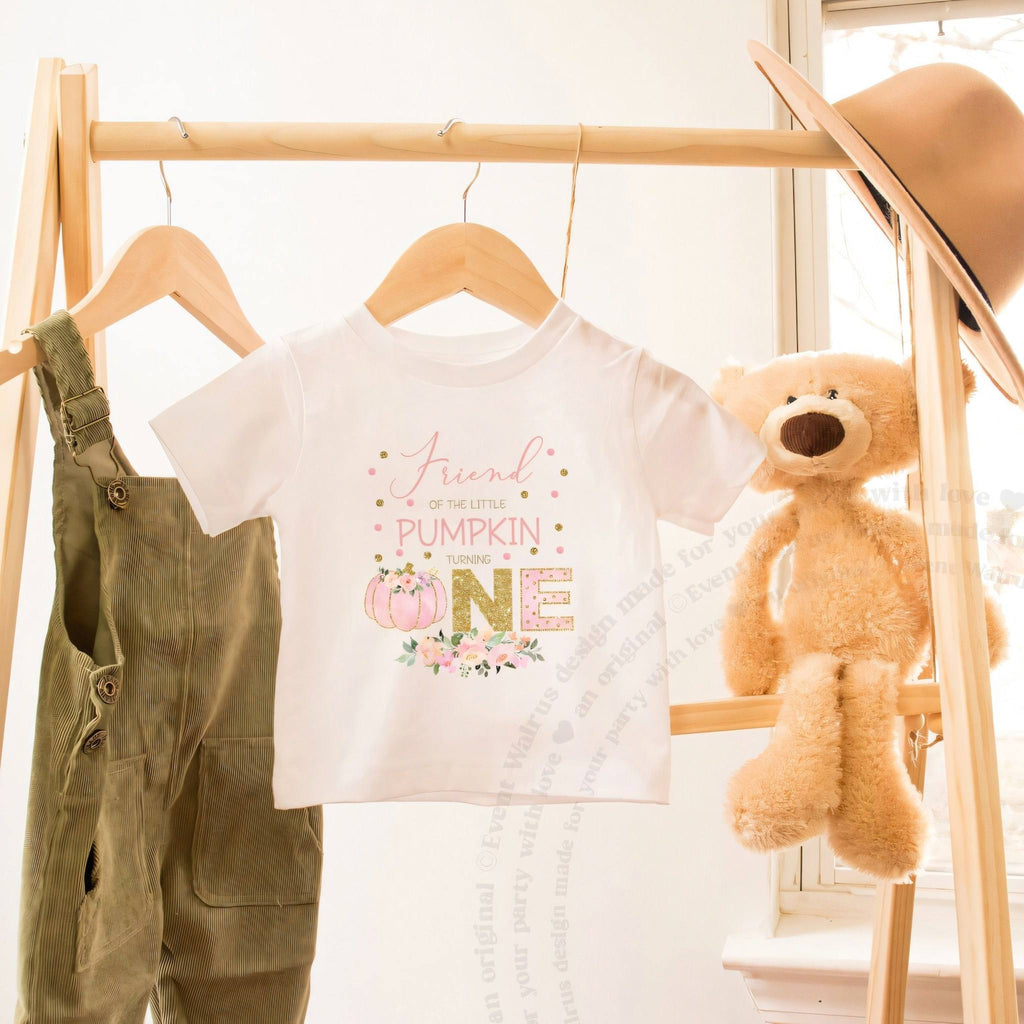 White Friend of the Little Pumpkin toddler tee on a wooden clothes rack beside a teddy bear.
