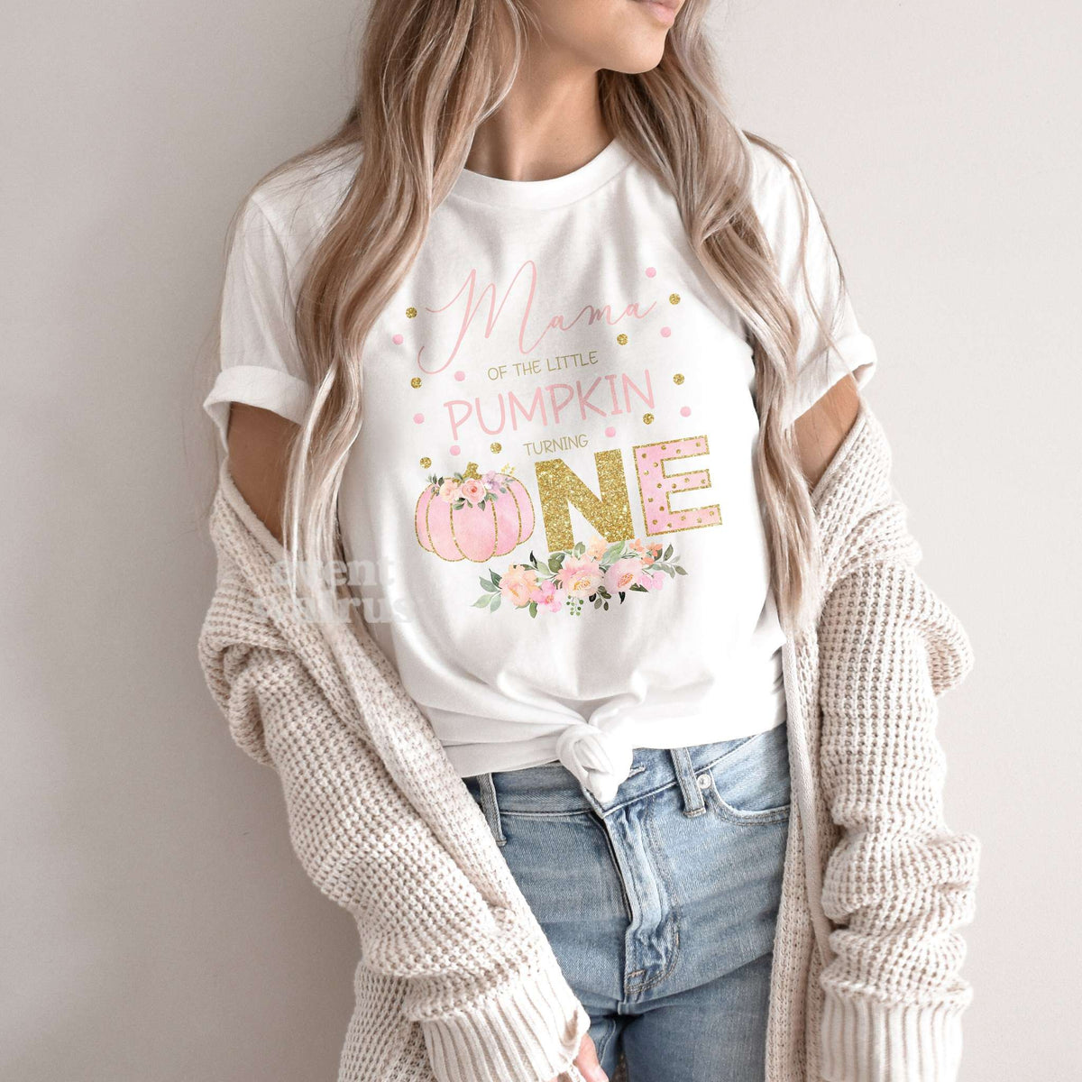 Woman in a knit cardigan wearing a white pink and gold Little Pumpkin Turning One shirt.