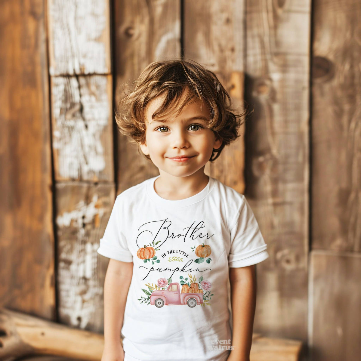 Toddler boy against a weathered wood wall in a white Brother of the Little Pumpkin tee.