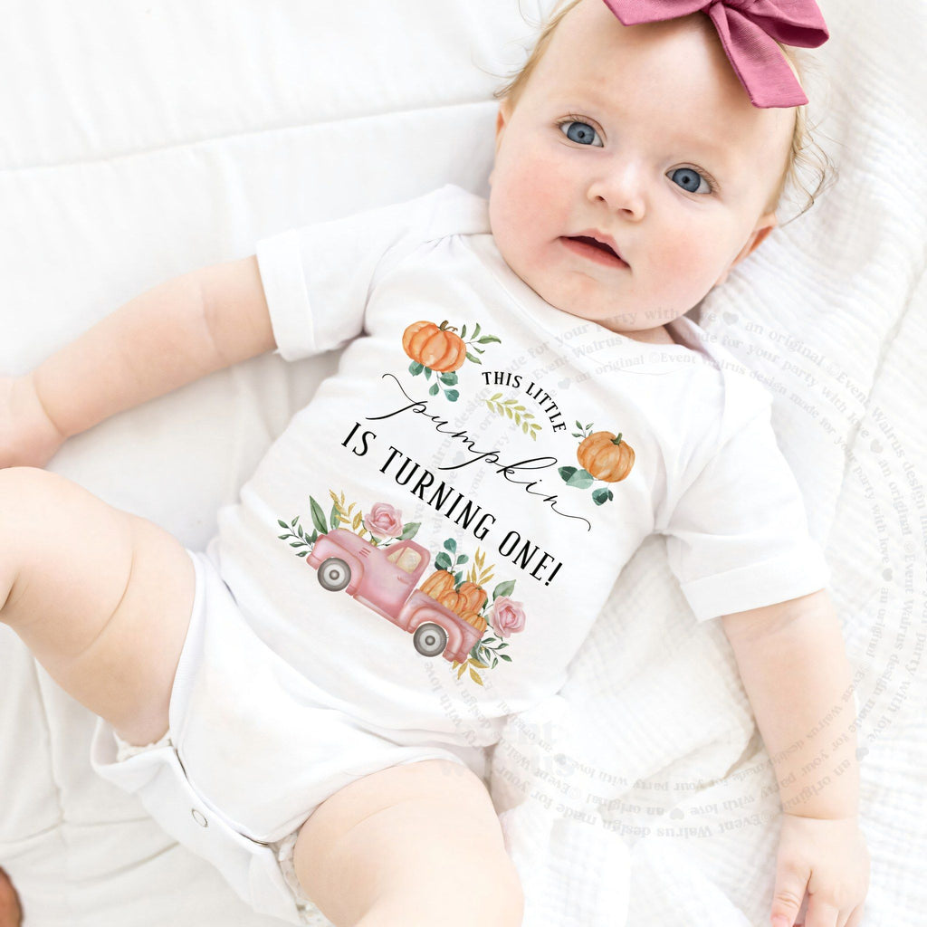 Baby girl with a pink bow lying in a white This Little Pumpkin Is Turning One bodysuit.