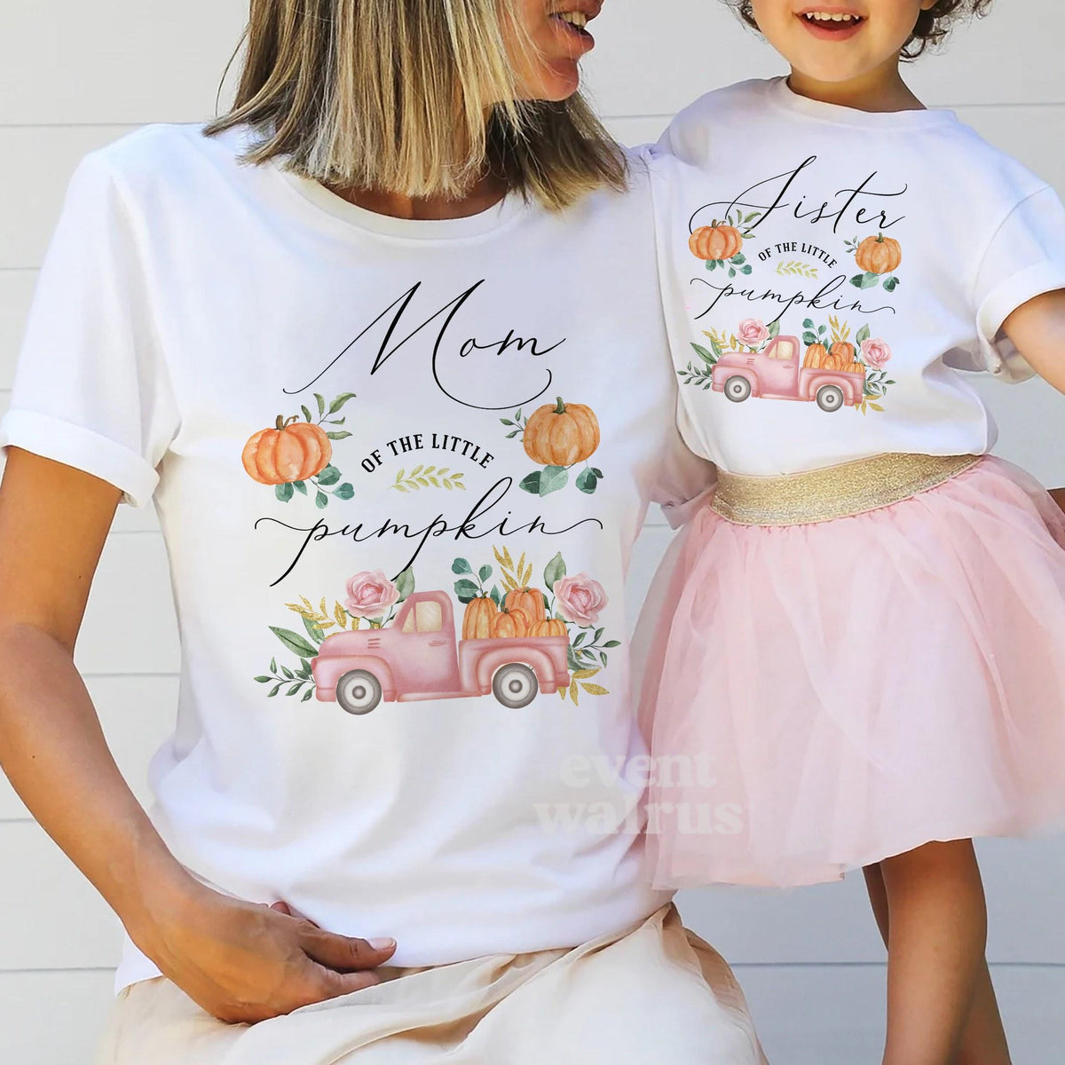 Little girl in a tutu holding Mom's hand, both in white pink pickup Little Pumpkin shirts.