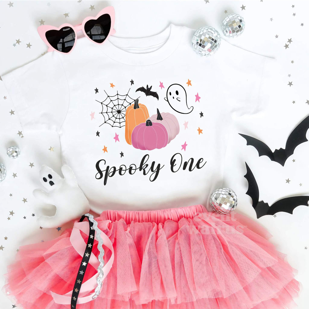White Spooky One toddler tee laid flat with a pink tutu, heart sunglasses and paper bats.