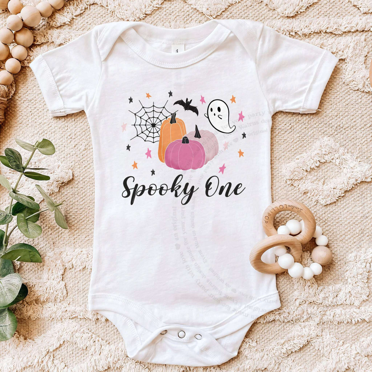 White Spooky One bodysuit on a beige blanket with a wooden teether.