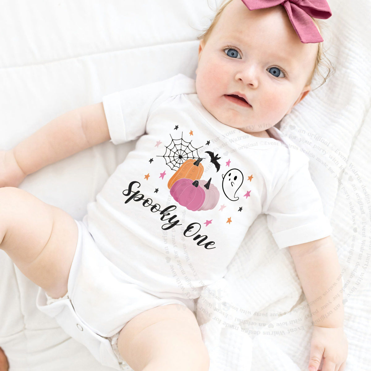 Baby girl with a pink bow lying in a white pink pumpkin Spooky One bodysuit.