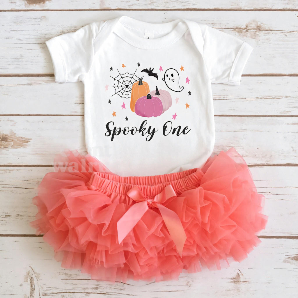 White Spooky One bodysuit laid flat with a coral tutu on whitewashed wood.