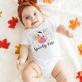 Baby girl in a rust headband lying among fall leaves in a white Spooky One bodysuit.