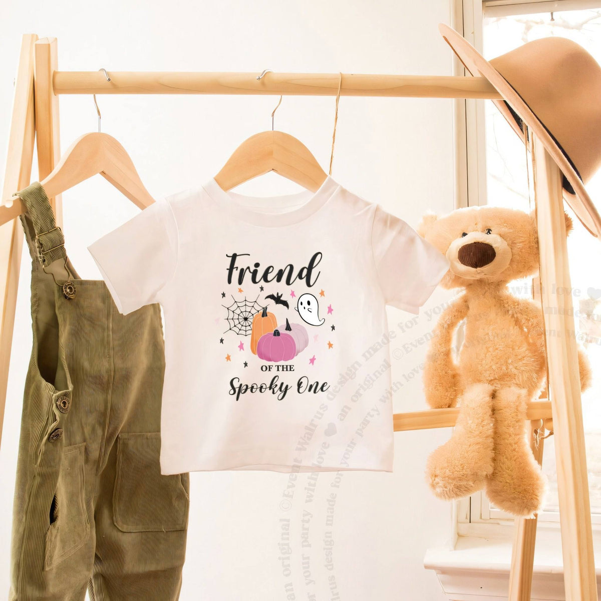 White Friend of the Spooky One toddler tee on a wooden clothes rack beside a teddy bear.