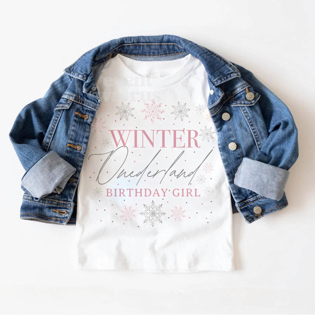White Winter Onederland Birthday Girl toddler tee laid on a denim jacket.