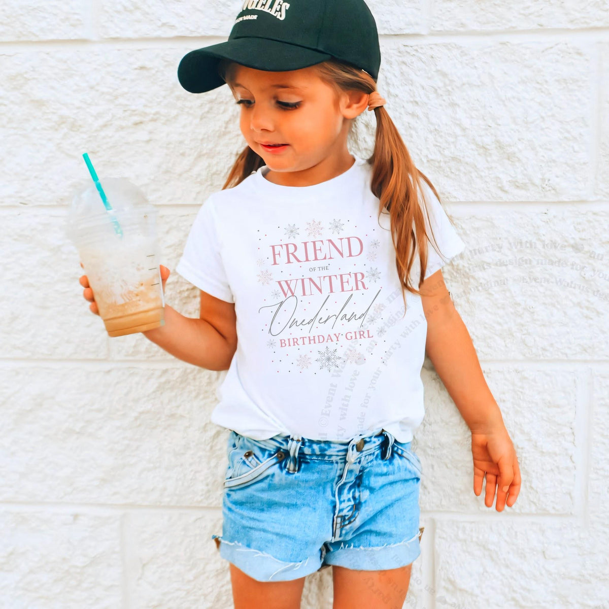 Girl in a ball cap holding a drink in a white Friend of the Winter Onederland shirt.