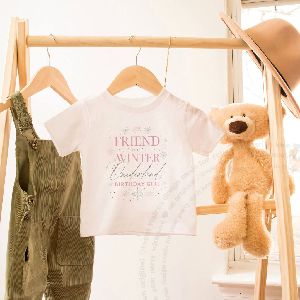 White Friend of the Winter Onederland toddler tee on a wooden clothes rack beside a teddy bear.