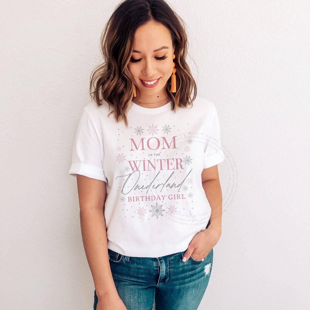 Smiling woman in jeans wearing a white Mom of the Winter Onederland Birthday Girl shirt with pink and silver snowflakes.