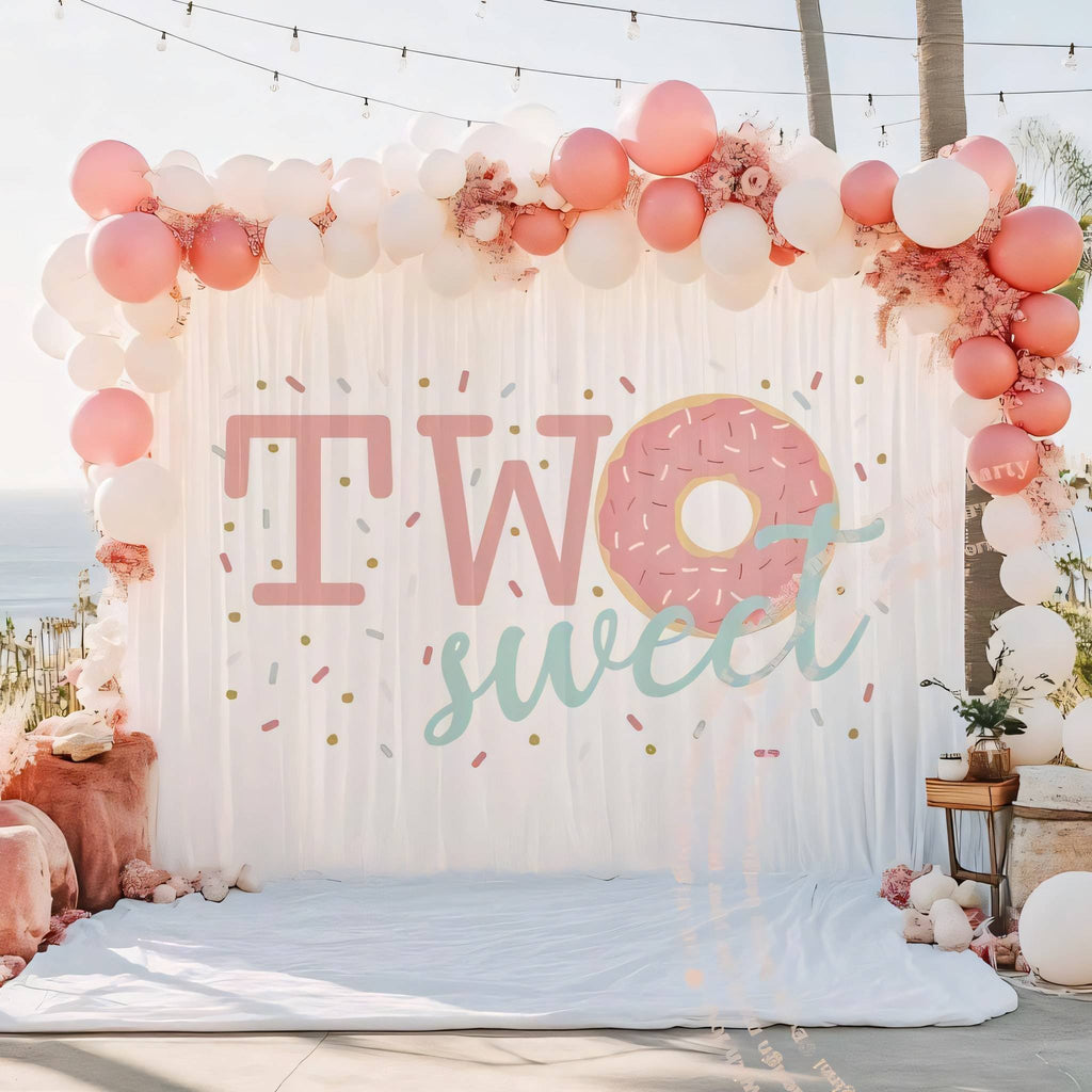 Donut two sweet backdrop under string lights with a pink and blush balloon garland.