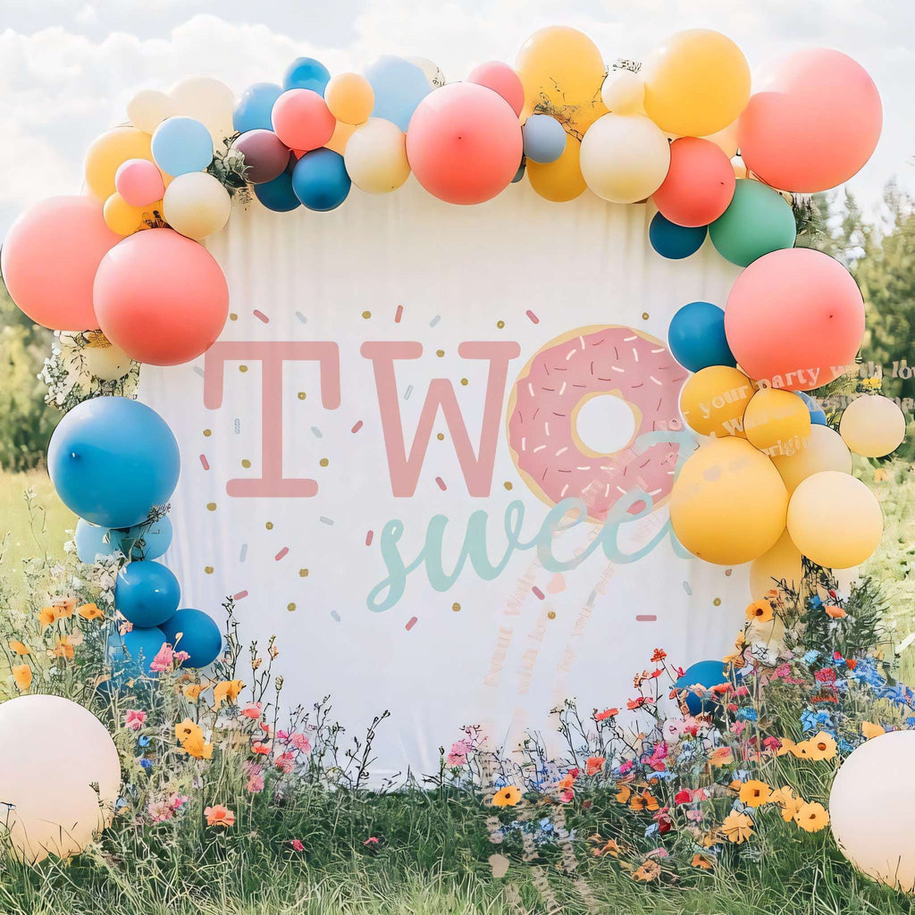 Pink donut two sweet backdrop in a wildflower field with a bright balloon arch.