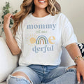 Woman sitting on a sofa in a white Mommy of Mr Onederful rainbow shirt.