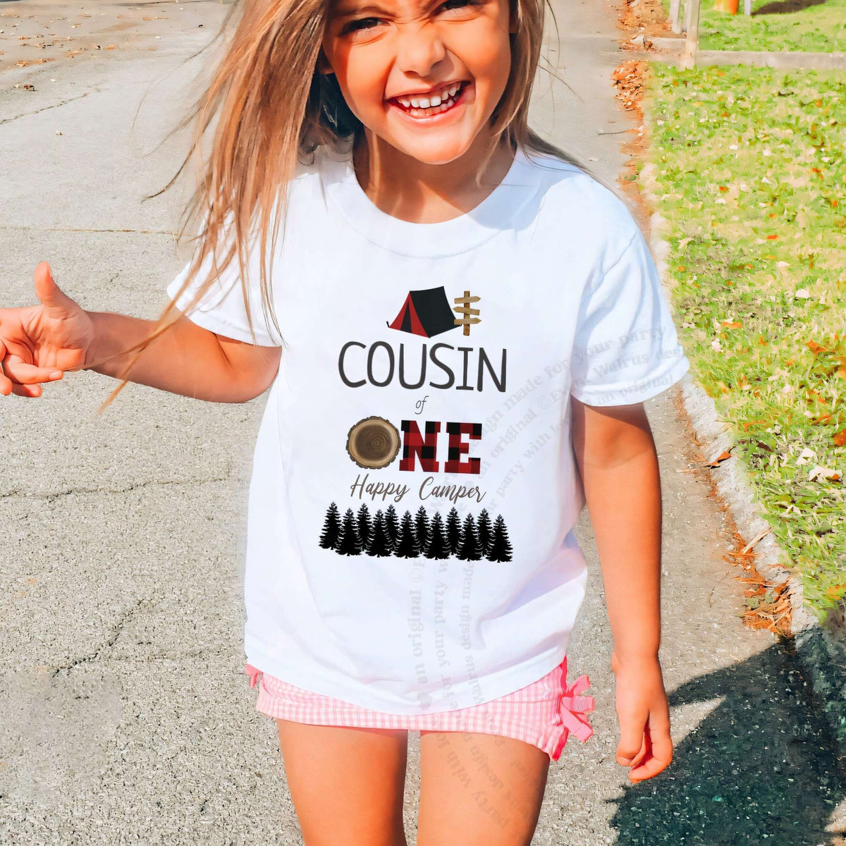 Laughing girl outdoors in a white Cousin of One Happy Camper kids tee.