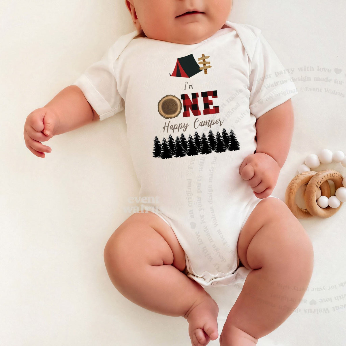 Baby lying on a white blanket in an I'm One Happy Camper red plaid bodysuit.