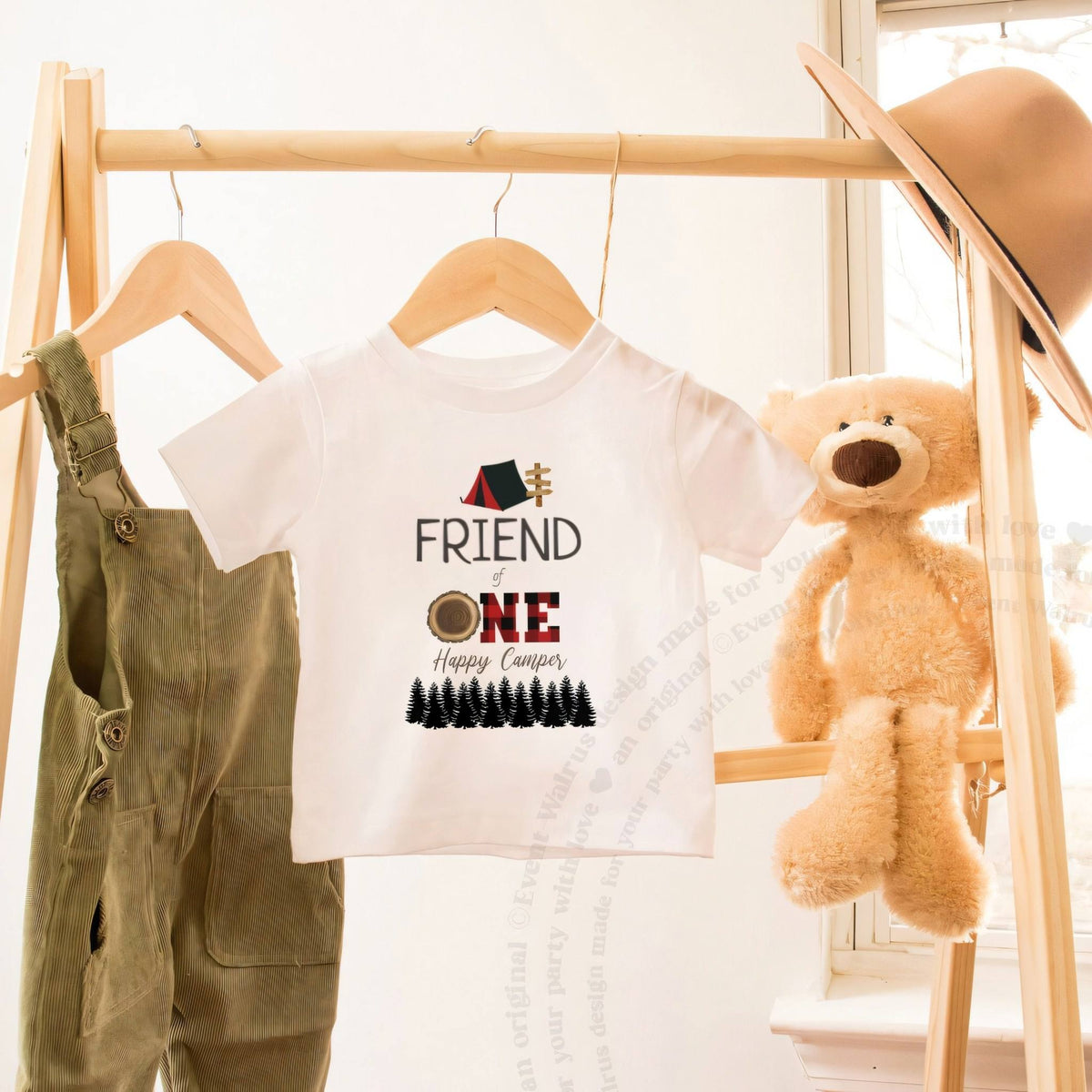 White Friend of One Happy Camper toddler tee on a wooden clothes rack beside a teddy bear.