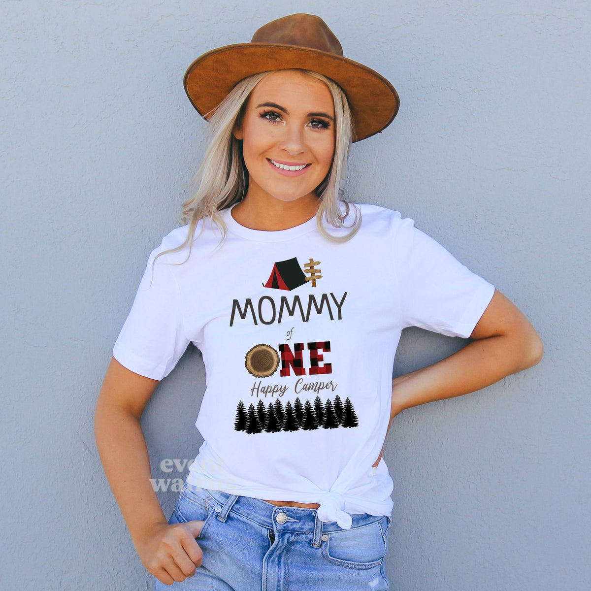 Smiling woman in a brown hat wearing a white Mommy of One Happy Camper shirt with a red plaid ONE.