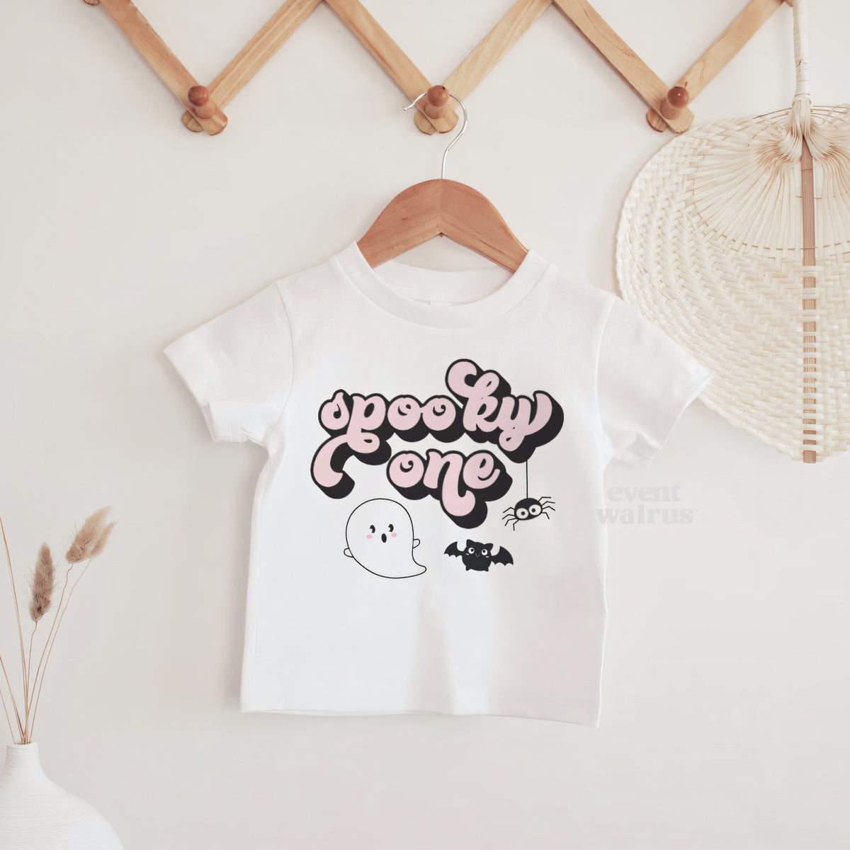 White Spooky One baby tee hanging on a wooden peg rail.