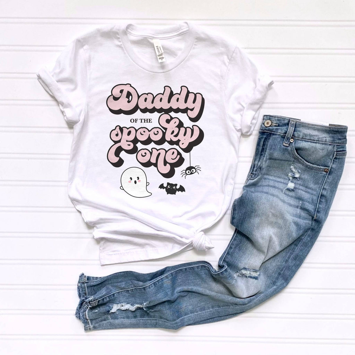 White Daddy of the Spooky One tee laid flat beside jeans.