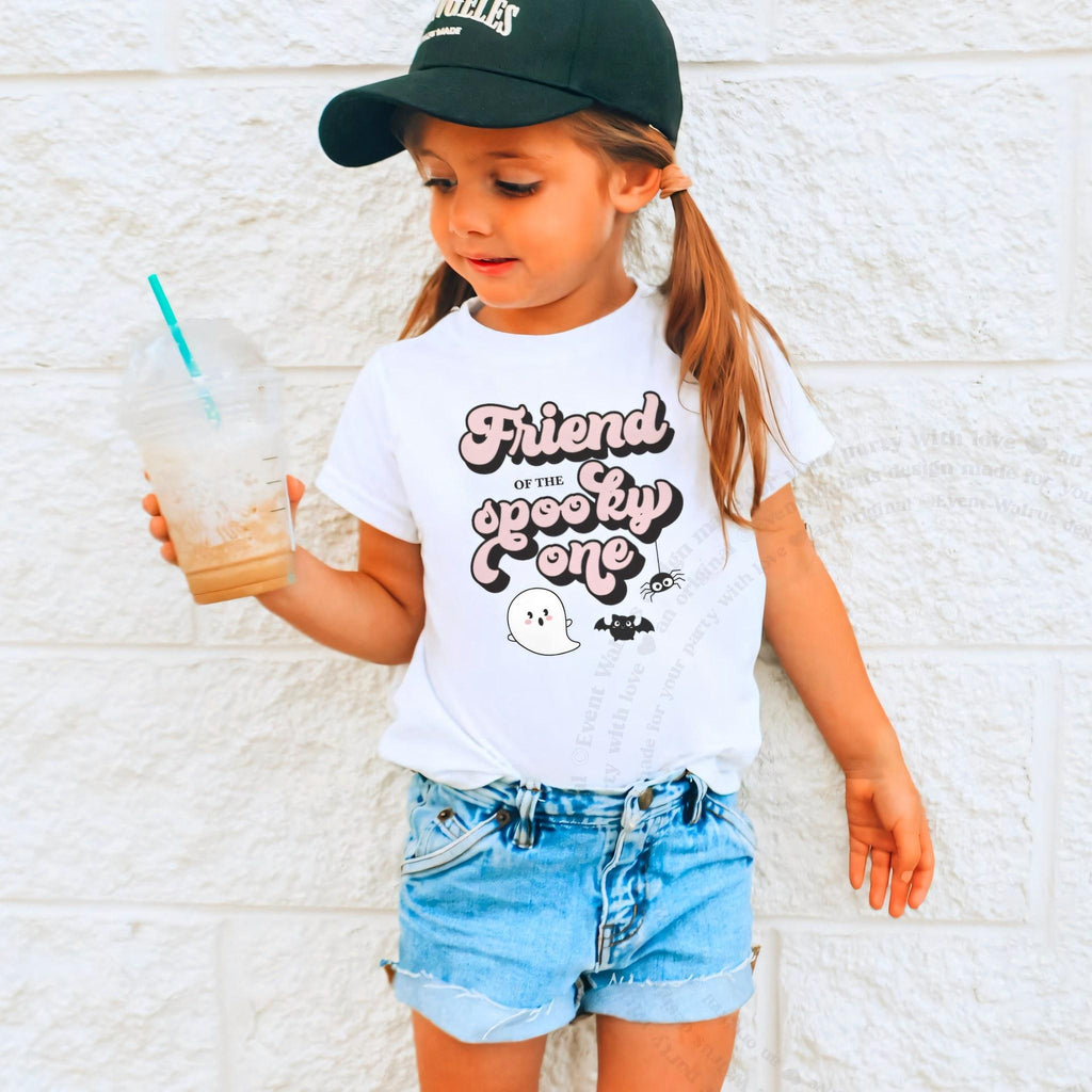 Girl in a ball cap holding a drink in a white Friend of the Spooky One shirt.