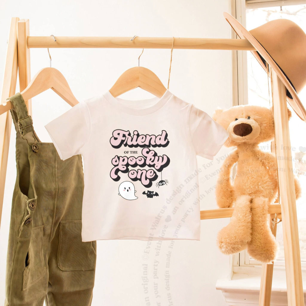 White Friend of the Spooky One toddler tee on a wooden clothes rack beside a teddy bear.