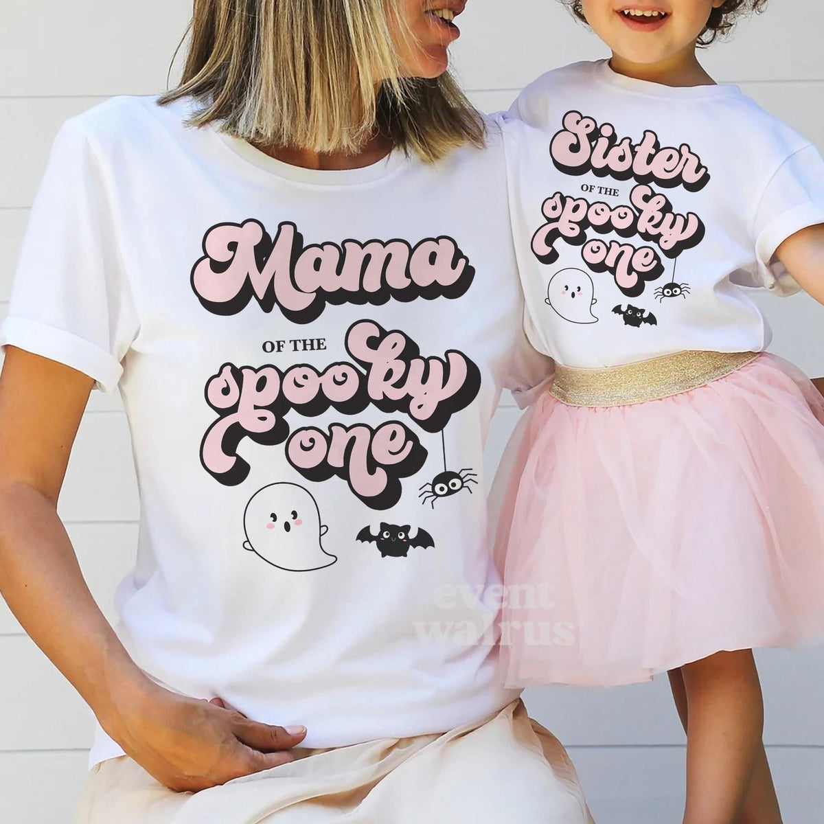Mom holding hands with her little girl in a tutu, in white Mama and Sister Spooky One shirts.