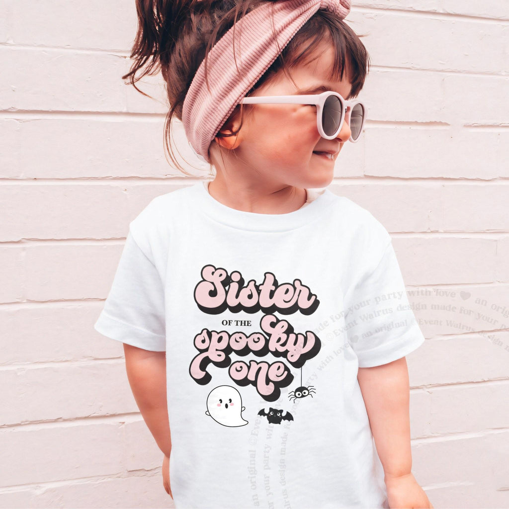 Girl in sunglasses and a pink headband wearing a white Sister of the Spooky One shirt.