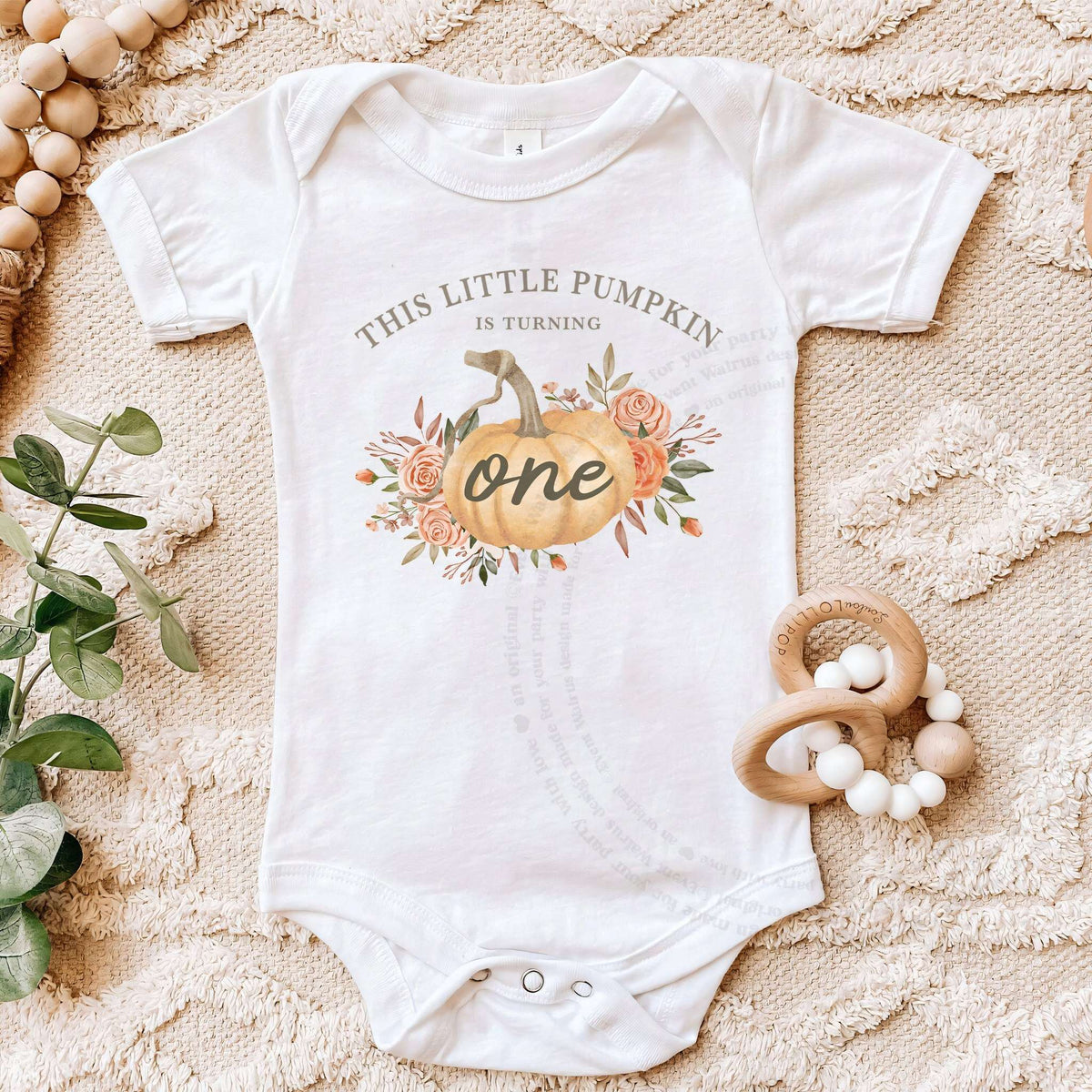 White Little Pumpkin bodysuit on a beige blanket with a wooden teether.